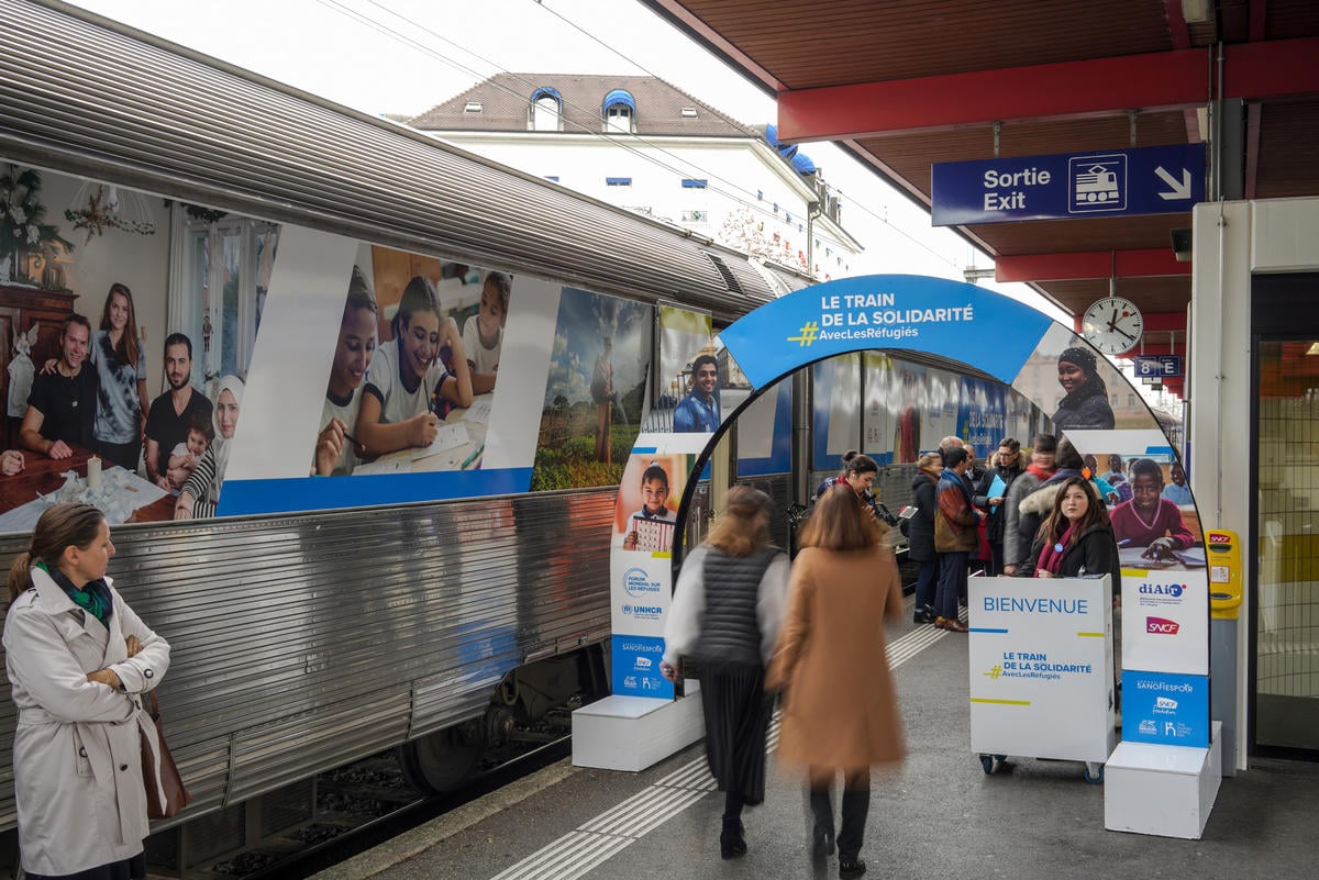 People walk past a train decorated with photos of refugees.