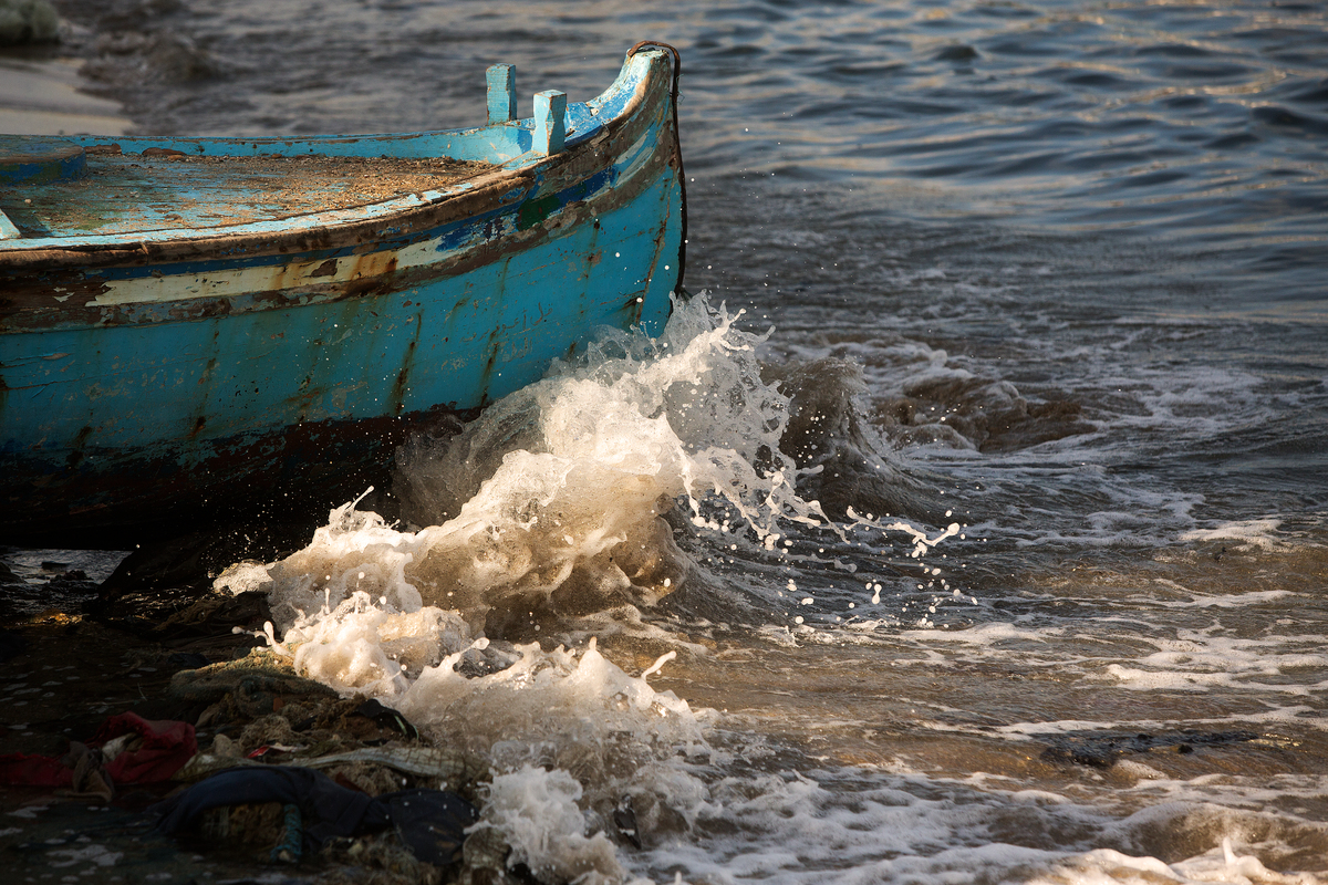 Waves crash against the bow of a teal fishing boat