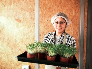 A woman wearing a hair net carries a tray of microgreens