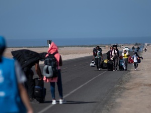 Refugees walk on a highway, with the sea in the background