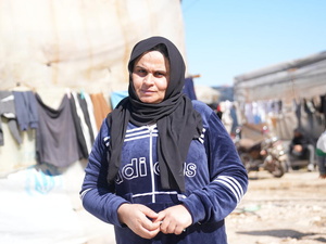 A woman stands outside in front of lines of washing and a UNHCR shelter