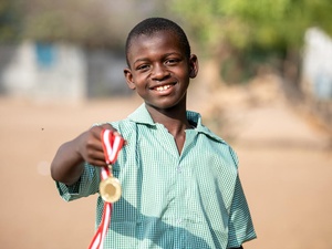 A 14-year-old Somalian boy poses outside, smiling and holding a medal