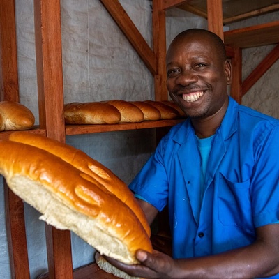 A refugee man holding fresh baked bread smiles for the camera, in the DR Congo.