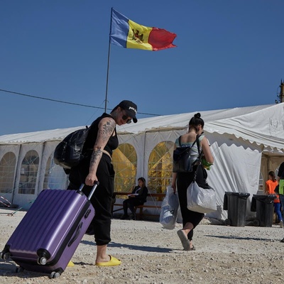 People carrying bags and pulling suitcases walk towards a large tent with a Moldovan flag flying above it