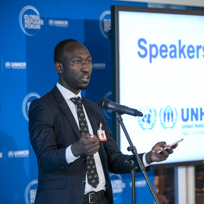 A man gives a speech, behind him a sign reads ' Speakers' Corner'