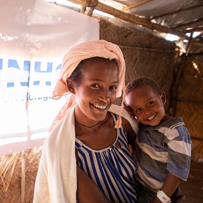 A mother holds her young son inside a UNHCR shelter. Both smile for the camera.