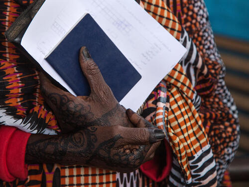 Folded hands hold blue and white document papers.