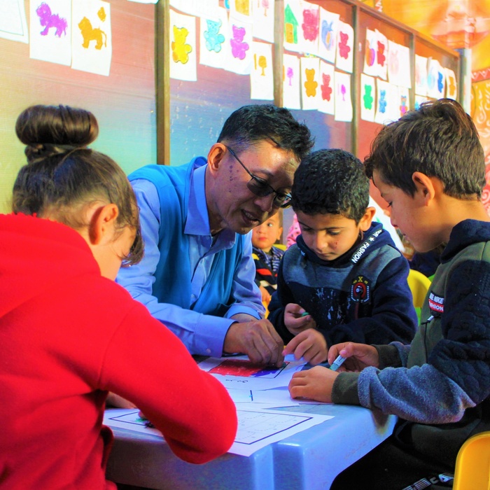 Mr. Wanchai Tachavejnukul sitting at a table, surrounded by children.