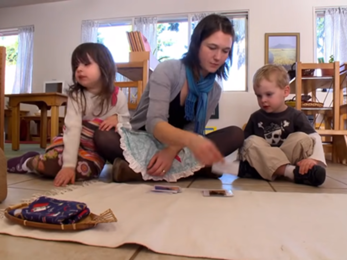 A woman sitting on the floor and playing with two young children.