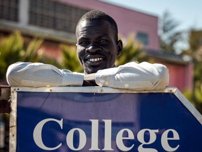A young man poses, leaning against a sign that reads "College of law"