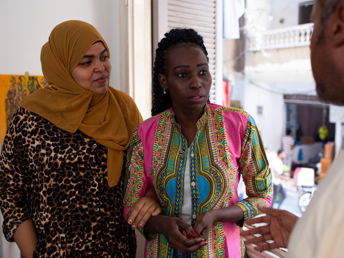 Two women link arms and listen to a man talking.