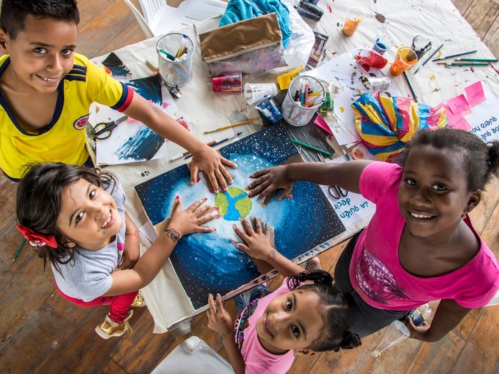 Four children hold their hands over a child's drawing of the world. 