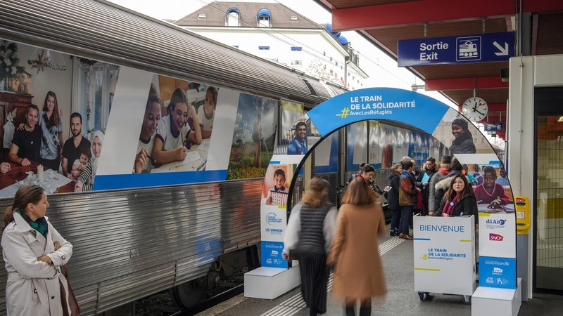 People walk past a train decorated with photos of refugees. 