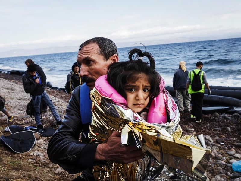 A young girl wrapped in a thermal blanket is carried by her father. 
