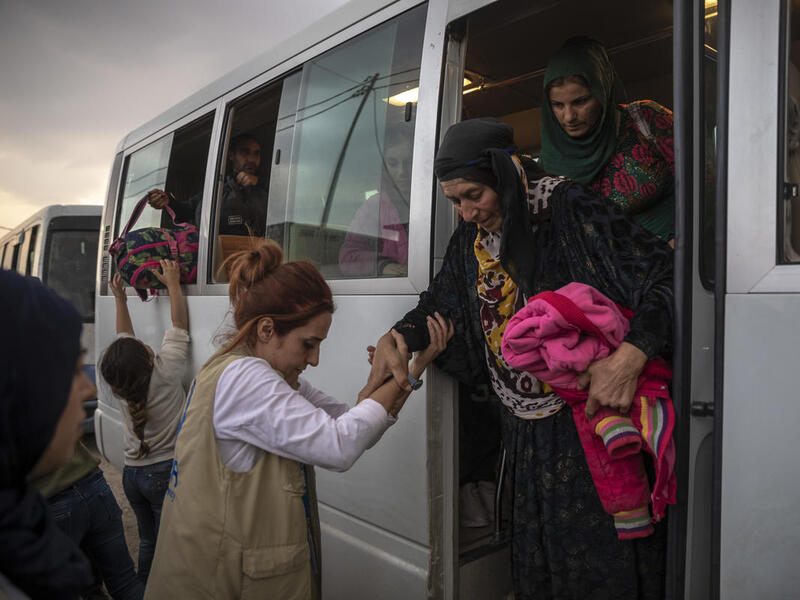 A UNHCR staff member helps an elderly Syrian refugee woman to step down from a bus. 