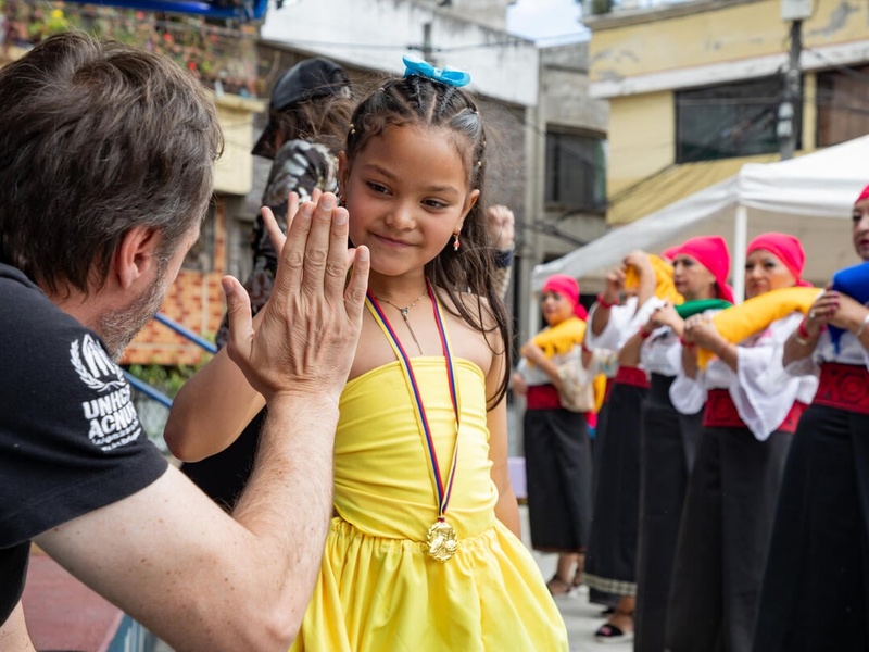 A UNHCR representative high-fives a young girl in a yellow dress