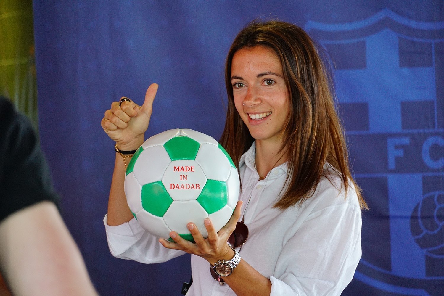 Aitana Bonmatí holding a hand-stitched football, smiling with a thumbs up