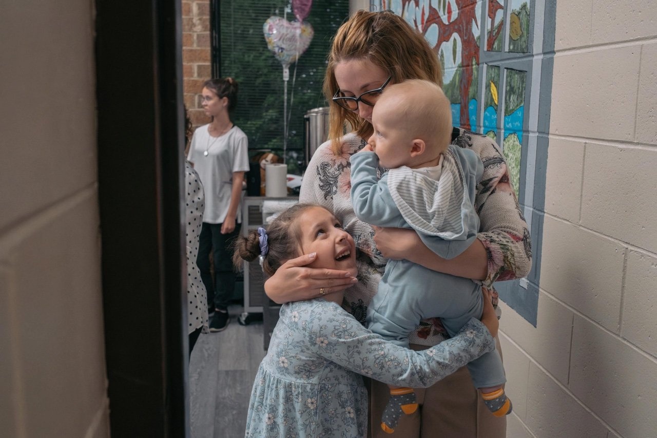 Una mujer abraza a sus hijos: un bebé y una niña pequeña