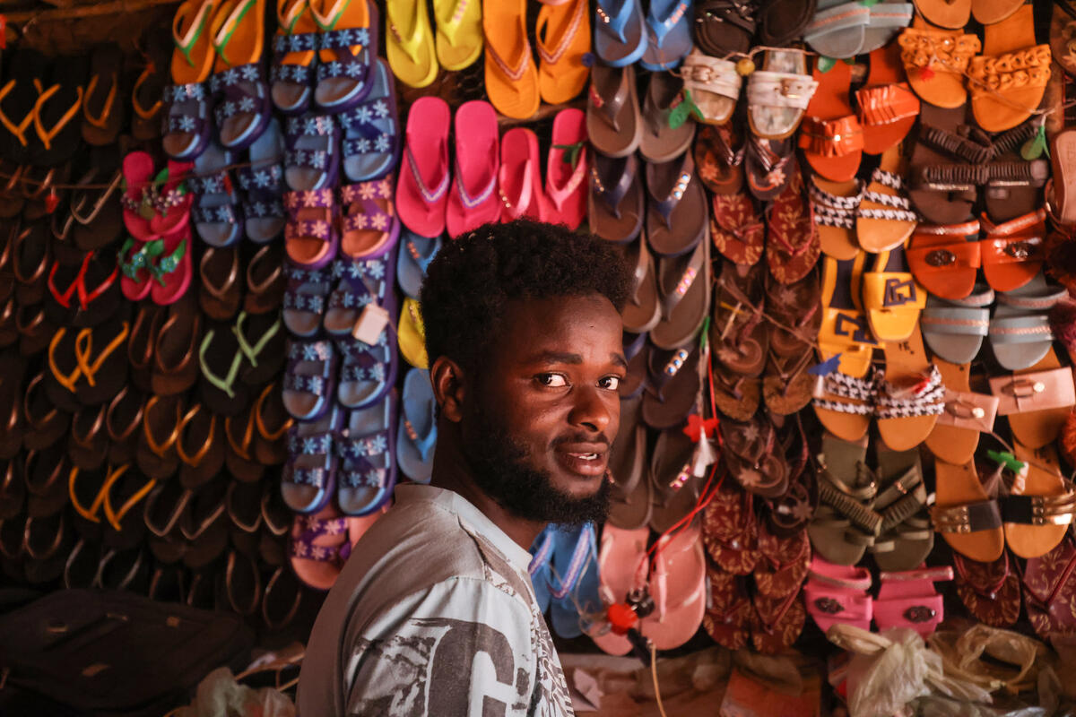 A Sudanese man in front of a wall of rows of colorful sandals