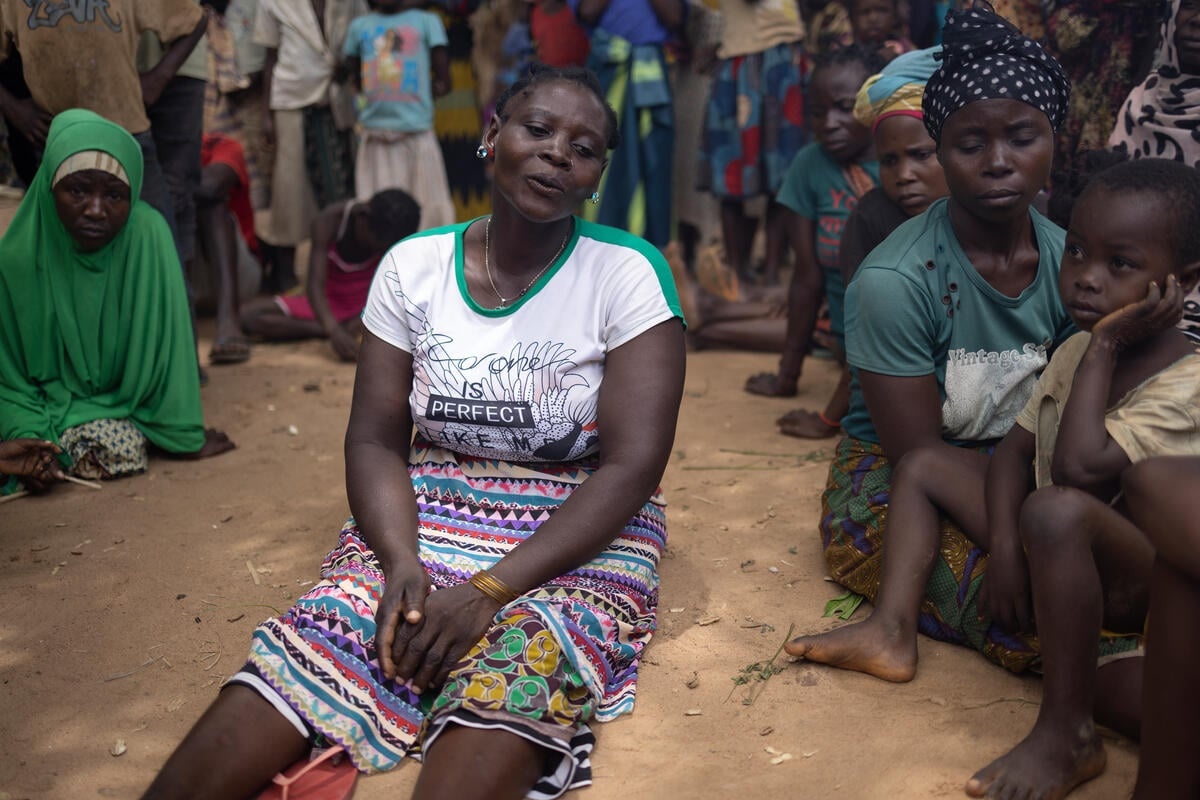 A woman sits on the dry ground, surrounded by people sitting and standing
