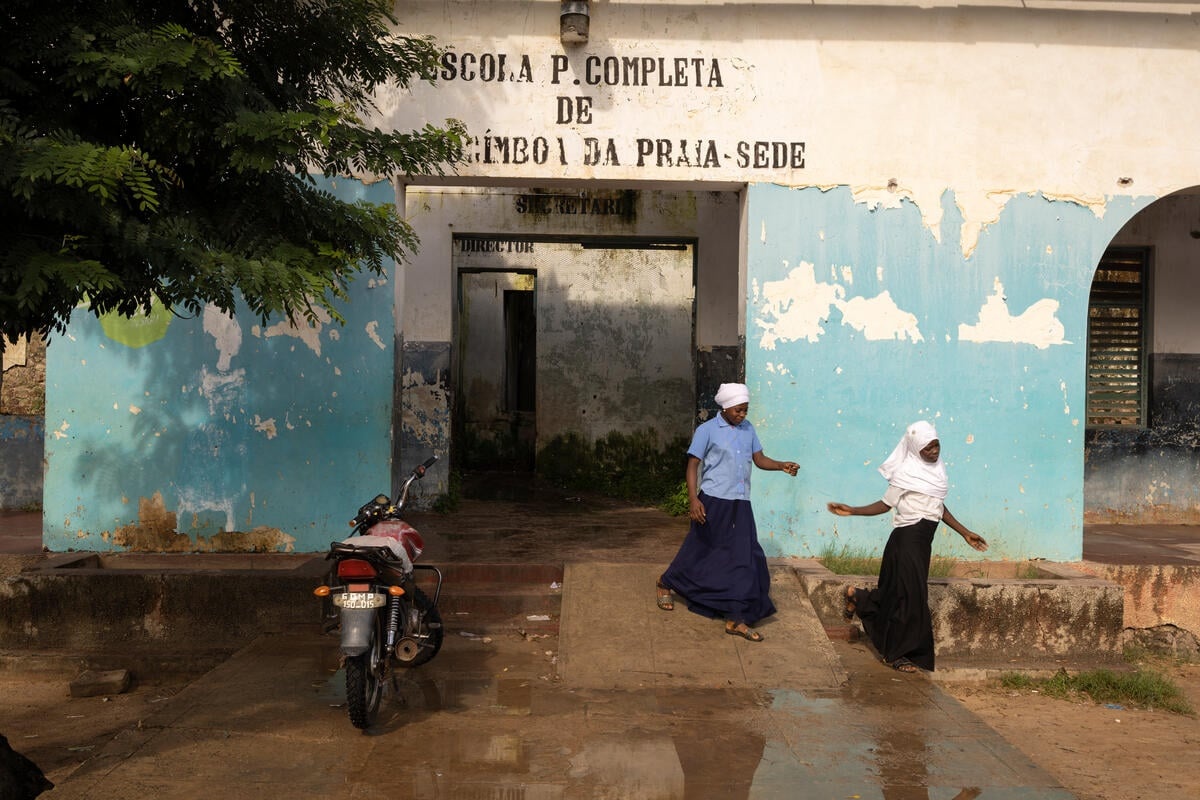 Two girls leave their school where there is a motorcyle parked out the front.