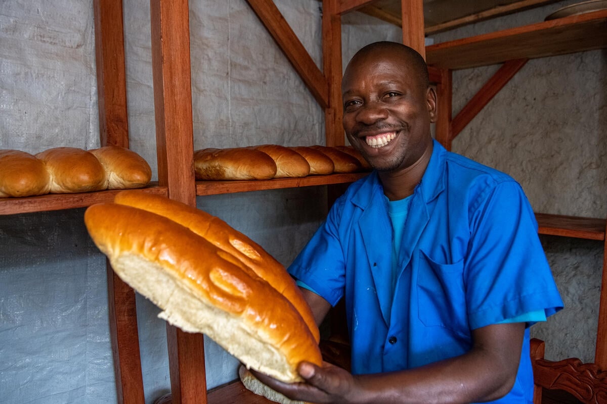 A refugee man holding fresh baked bread smiles for the camera, in the DR Congo.