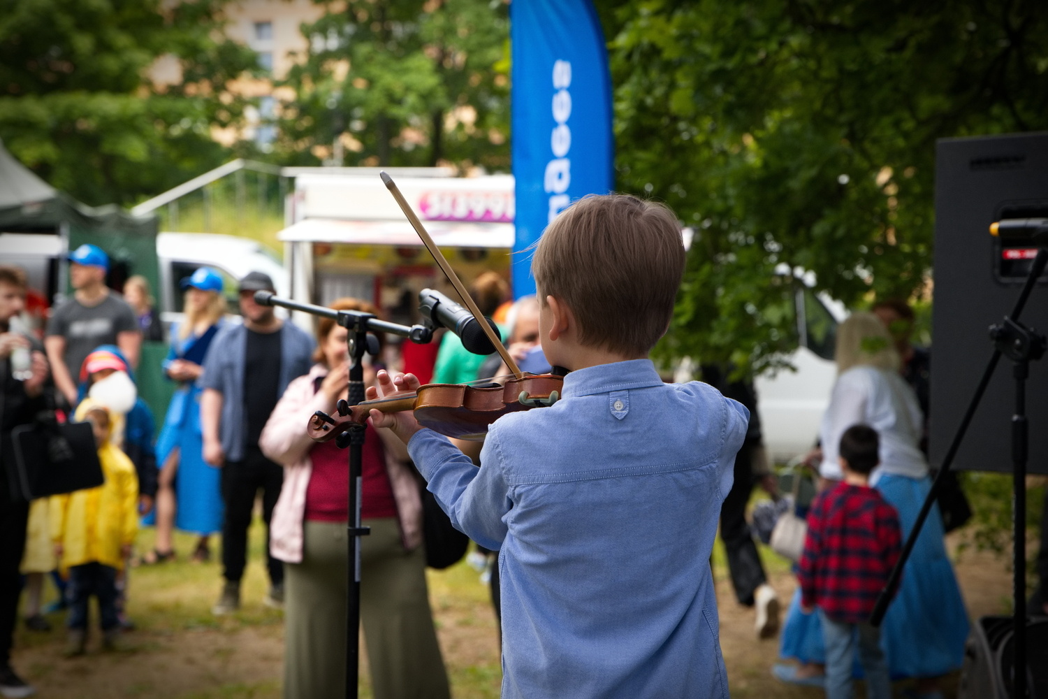 A young boy plays the violin at an outdoor event.