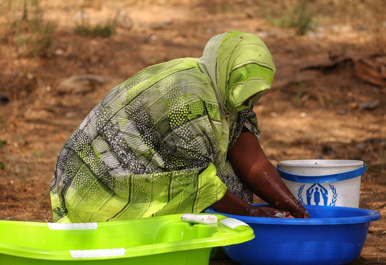 A woman washes clothes outdoors in a plastic basin.