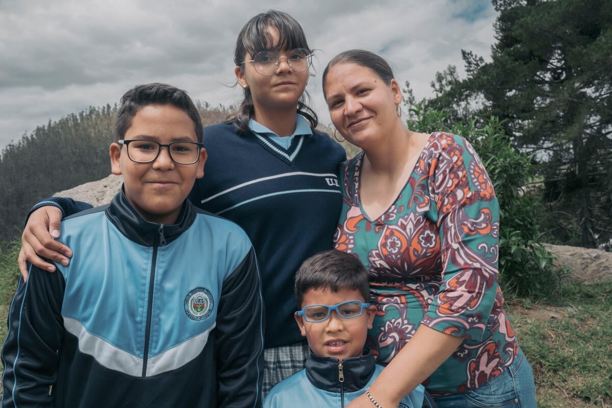 A boy with his two siblings and their mother outside with trees in the background