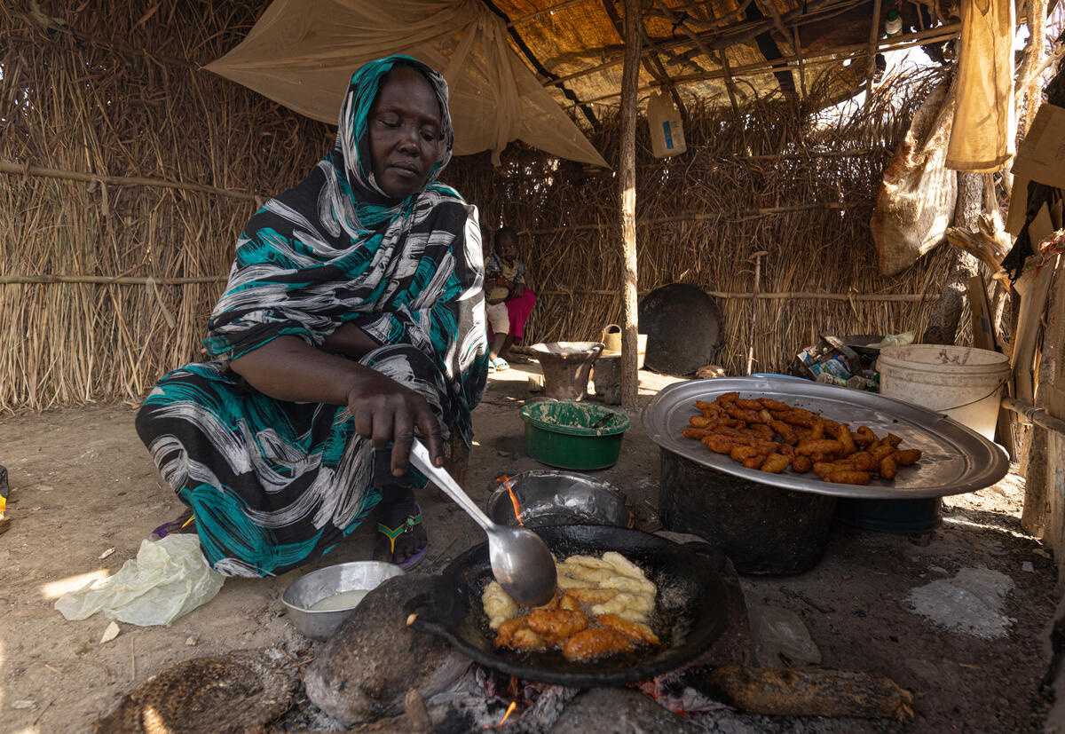 A woman squats on the floor in a shelter, cooking.