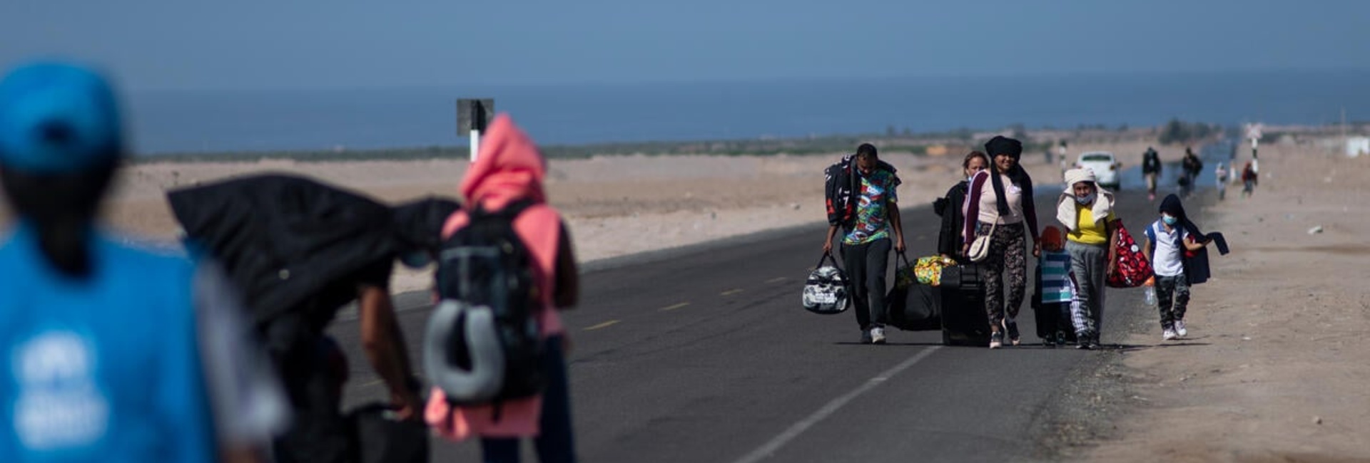 Refugees walk on a highway, with the sea in the background