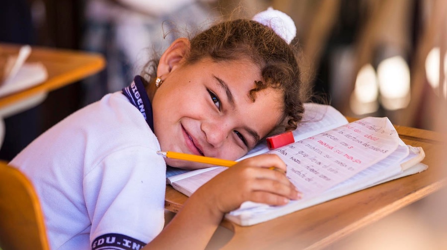 A girl smiles while leaning on her open notebook in a classroom at a school in Colombia.