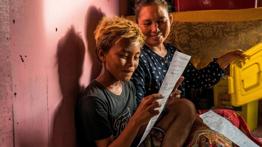 A young Filipino boy smiles as he reads his name on his birth certificate while his mother looks on. 