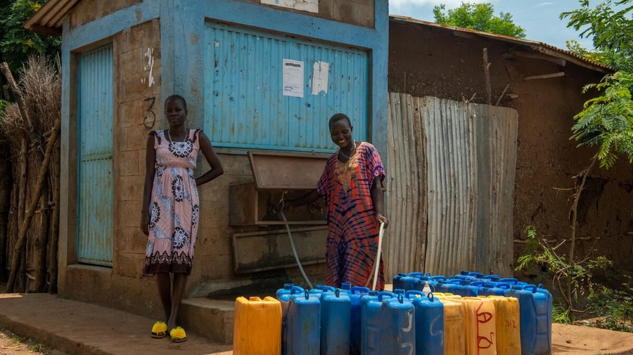 Two women fill jerry cans with water from an outdoor tap. 
