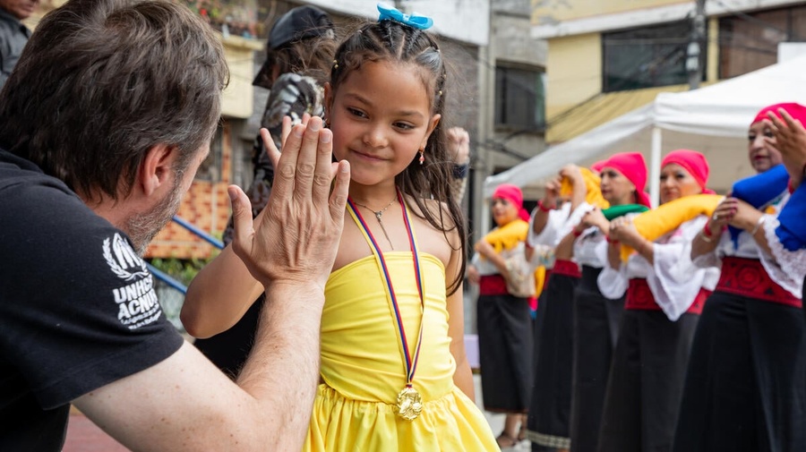 A UNHCR representative high-fives a young girl in a yellow dress