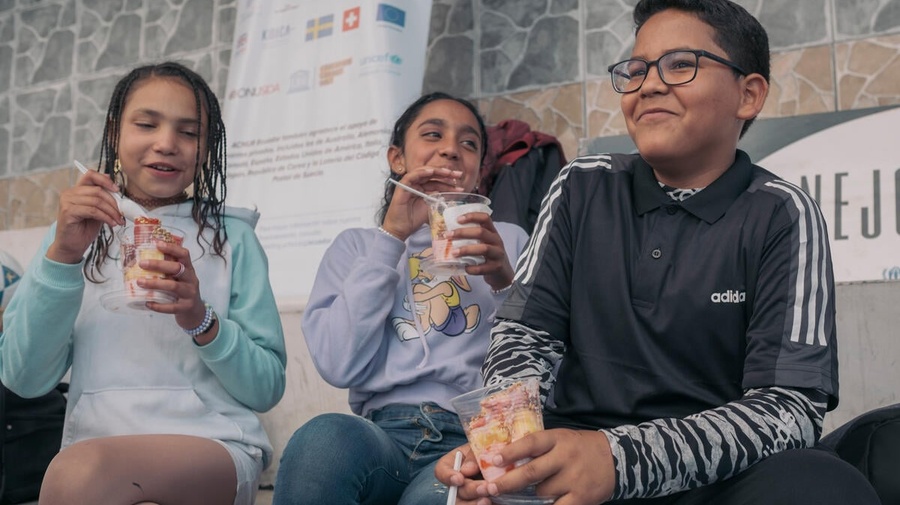 Three children laughing while eating dessert outside