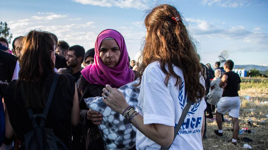 A UNHCR staff member distributes blankets to people waiting to cross the Greek-FYR Macedonian border.