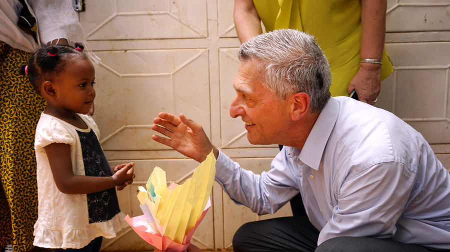 UN High Commissioner for Refugees Filippo Grandi (right) crouches to speak with a young refugee girl.