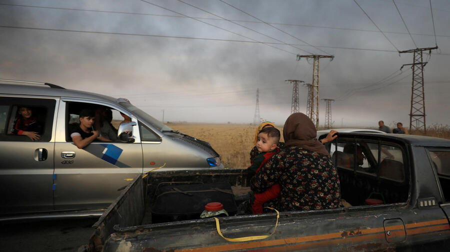 Syria. A woman with a baby sits at a back of a truck as they flee Ras al Ain town