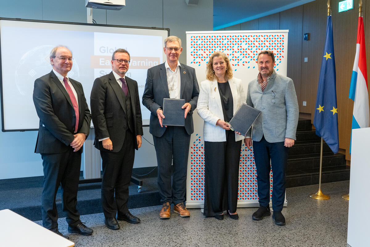 Quatre hommes et une femme regardent la caméra en brandissant deux documents.