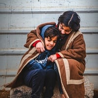 Een jonge Syrische vluchteling wikkelt zichzelf en haar jongere broertje in een deken terwijl ze buiten in de kou zitten in het vluchtelingenkamp Zaatari.