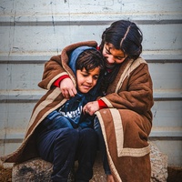 Une jeune réfugiée syrienne s'enveloppe avec son jeune frère dans une couverture alors qu'ils sont assis dehors dans le froid dans le camp de réfugiés de Zaatari.