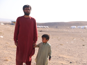 Un père et son jeune fils se tiennent dans un paysage aride avec des rangées de tentes à l'arrière-plan.