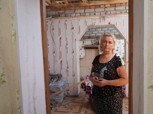 Une femme se tient dans une maison détruite.