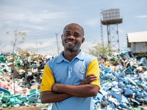 Un homme souriant se tient devant un énorme tas de déchets plastiques.