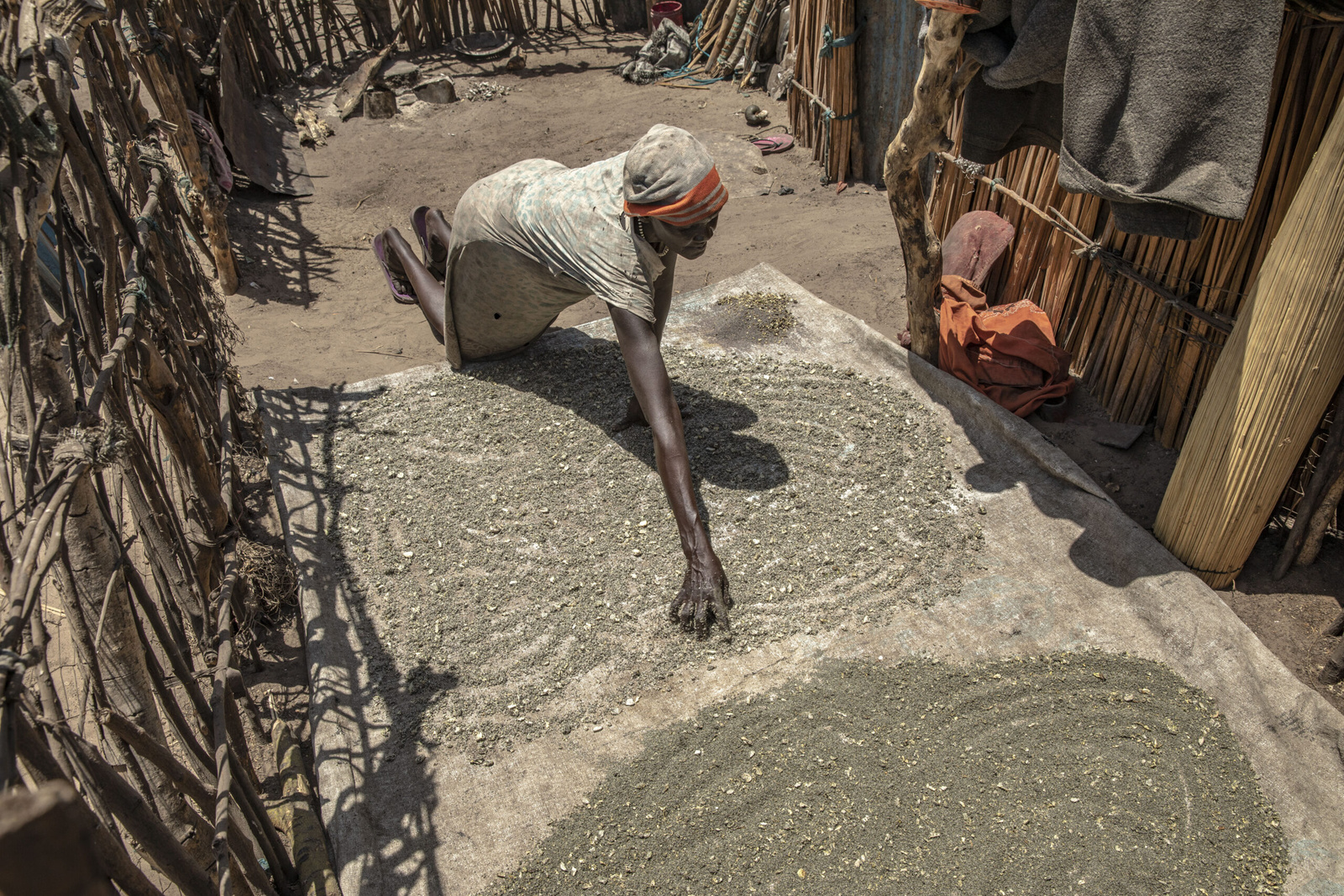 Een vrouw legt geplette waterlelies te drogen in de zon voor haar huis in het dorp Tong. © UNHCR/Andrew McConnell