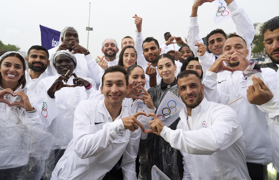 Un groupe de jeunes hommes et femmes vêtus de survêtements blancs font des émojis en forme de cœur avec leurs doigts.