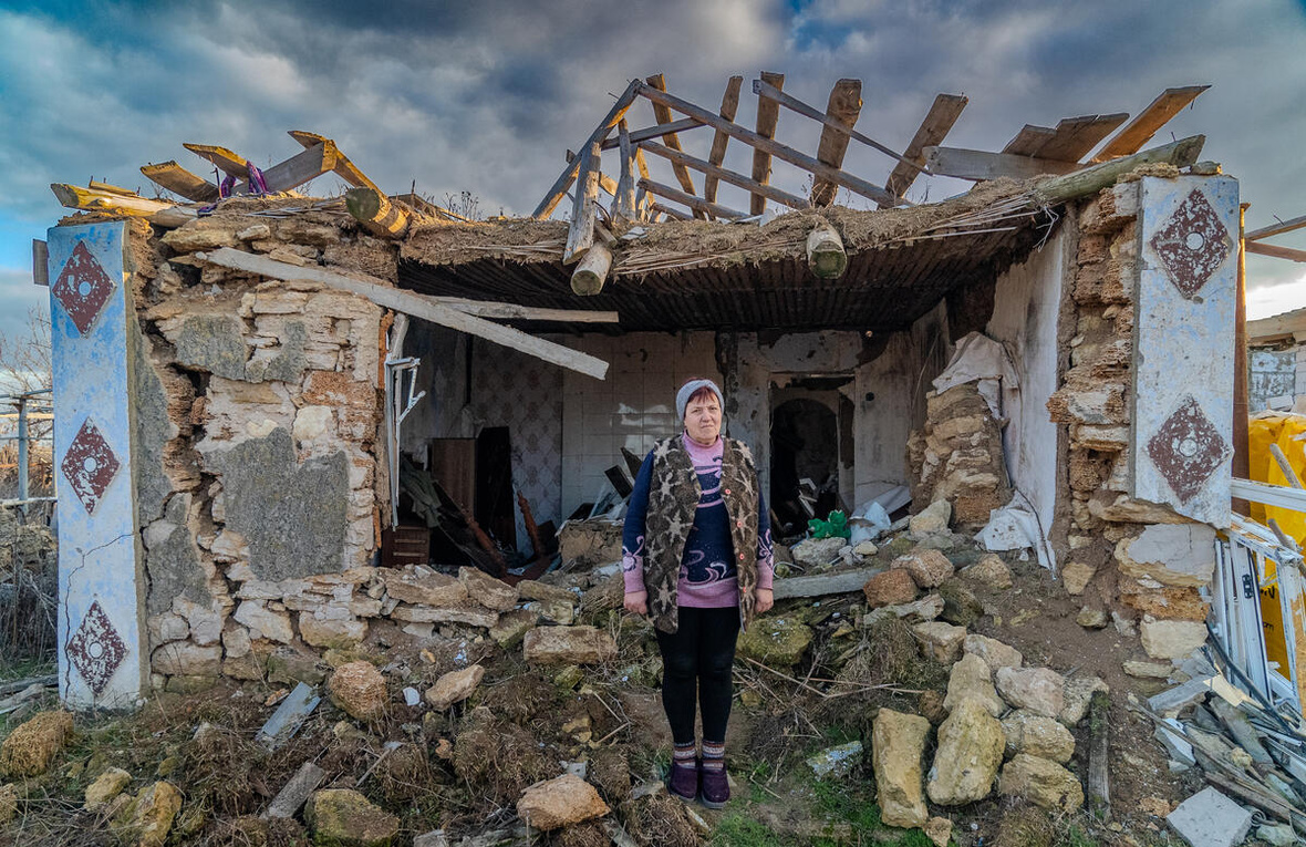 Valentyna Zavadska, 64, voor het puin van haar huis nabij Mykolaiv, dat in maart 2022 door artillerie werd vernietigd. Ze kreeg steun van een lokale NGO en partner van UNHCR om een aangrenzend gebouw op te knappen om in te wonen.