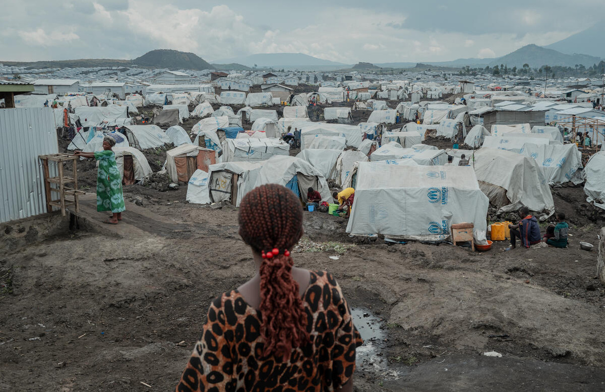 Vue arrière d'une femme debout sur un sol boueux devant des centaines de tentes qui s'étendent jusqu'à l'horizon.