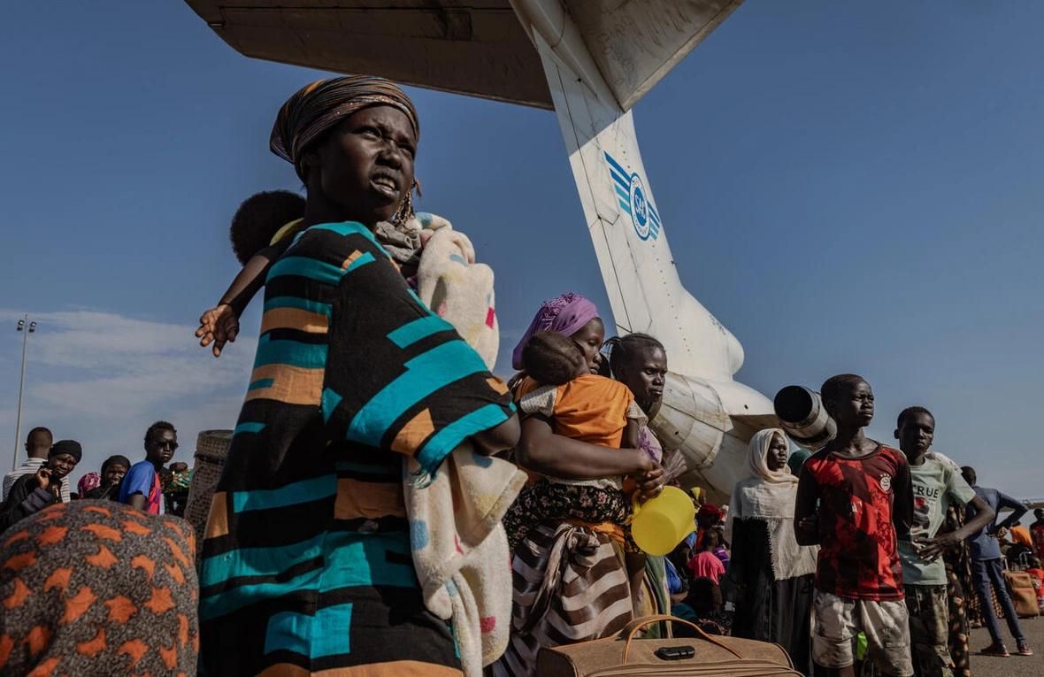 Une femme et sa petite fille attendent avec des centaines de réfugiés sud-soudanais qui sont rentrés à l'aéroport de Palouch dans l'Etat du Haut-Nil, au Sud-Soudan, pour embarquer dans l'un des avions-cargos transportant des personnes vers différentes régions du pays. HCR/Andrew McConnell